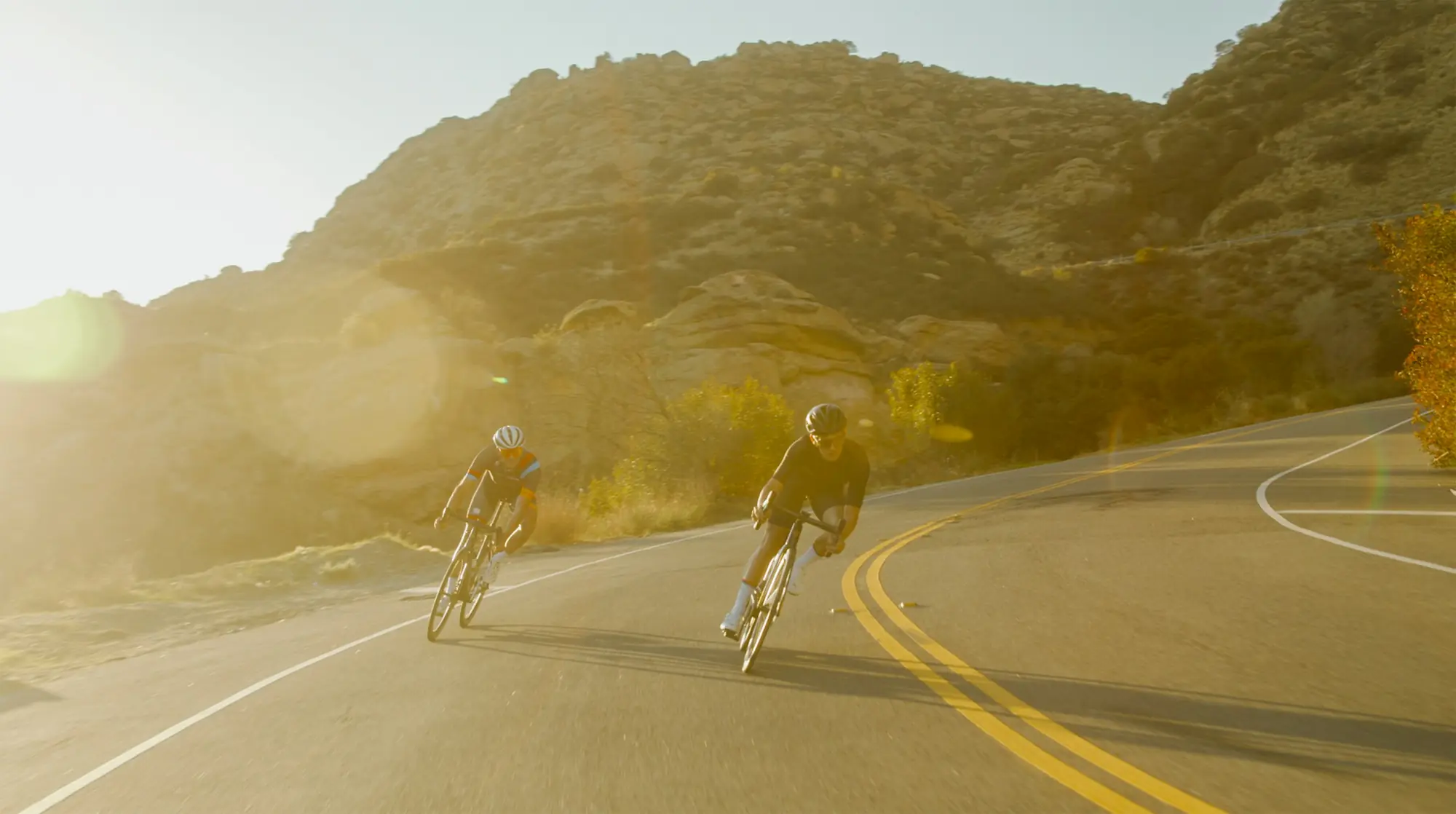 Deux coureurs dans une descente en courbe, à contre-jour.